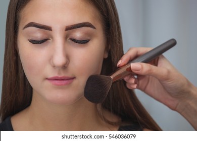Master inflicts brush powder on the face of the girl, completes the day make-up in a beauty salon. Professional skin care.