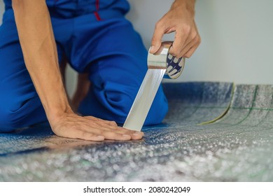 Master installs the overlapping thermal insulation in the room. Floor heating installation. Male hand holds reinforced tape. Repair in the apartment, floor insulation - Shutterstock ID 2080242049