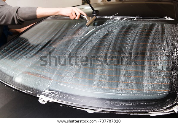 Master installs a\
tint film for the car glass with a hairdryer and spatula with glare\
of light. Concept\
tinting