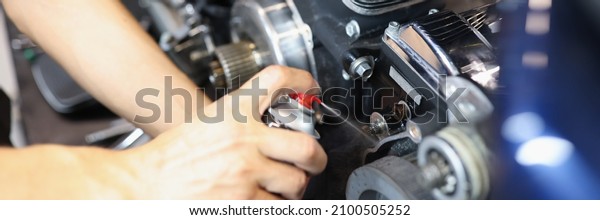 Master locksmith puffs liquid on\
motorcycle engine in garage. Motorcycle maintenance\
concept