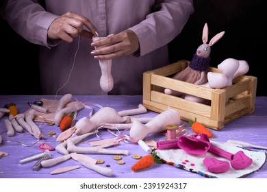 Master makes a handmade soft textile toys (dolls) of pink bunny on purple wooden table. Workflow. Shaping the doll's body.