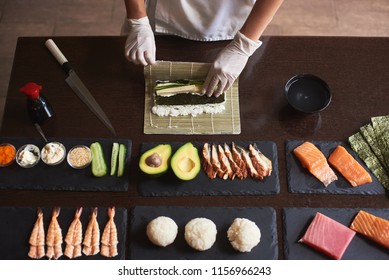 Master making a sushi roll with nori, rice, cucumber and omelet using bamboo mat. Closeup view of process. View from the top - Powered by Shutterstock