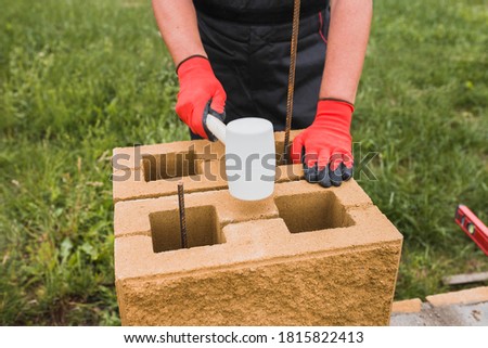 Master mason knocks with a rubber mallet on a stone block - construction of a fence post from a concrete block