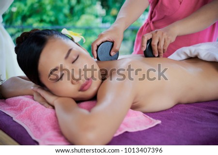 Master massaging body of female client with hot basalt stones