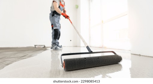 Master with needle roller for new screed concrete with self leveling cement mortar for floors. Concept building renovation home. - Shutterstock ID 2298085413