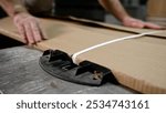 The master packs the goods in cardboard, close-up. Factory worker tightening a strap around cardboard on a metal table, ensuring secure packaging for distribution. Furniture production concept.