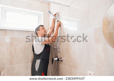 A master plumber installs a shower head in the bathroom. Professional assistance in the repair and assembly of plumbing.