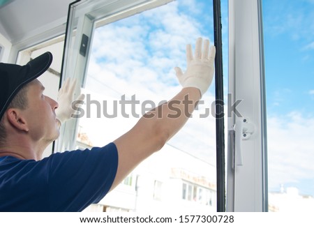 master in protective gloves, changing a double-glazed window in a plastic window, side view, against the blue sky