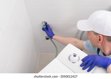 the master in protective gloves, installs the washing machine, connects it to the water supply and drainage systems
