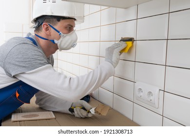 a master in a protective uniform and gloves, hermetically wipes the cracks with light brown putty, on a light apron, lined with white tiles