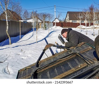 The master repairs a car trailer using electric arc welding. An elderly male worker sparks during steel welding on a spring sunny day against the backdrop of snow.