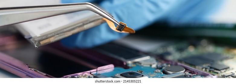 Master In Rubber Gloves Holding Microchip Over Broken Phone In Workshop