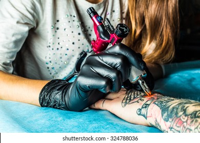 Master tattoo draws the orange paint on the clients tattoo. Tattoo artist holding a pink tattoo machine in black sterile gloves and working on the professional blue mat.  - Shutterstock ID 324788036
