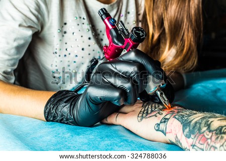 Master tattoo draws the orange paint on the clients tattoo. Tattoo artist holding a pink tattoo machine in black sterile gloves and working on the professional blue mat. 