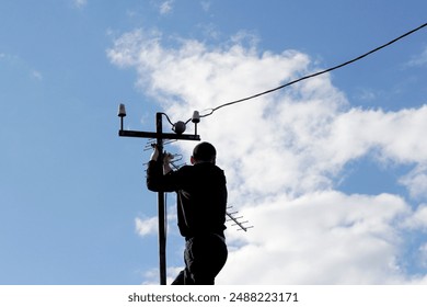 Master technician installs television antenna on rooftop. Expert setting up communication antenna under clear sky. Skilled technician mounting TV antenna with blue sky background. - Powered by Shutterstock