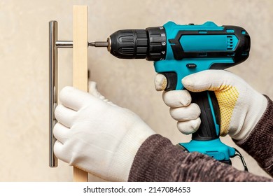 The master uses a cordless screwdriver to screw the handle to the cabinet door