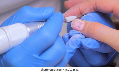 The master uses an electric machine to remove the nail polish on client hands during hardware manicure in the salon. Beauty and nail care concept - Shutterstock ID 750108643