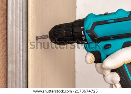 The master uses an electric screwdriver to attach the drywall to the metal profile