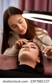 master using brush for combs the eyelashes of the client after the eyelash extension procedure. Cosmetology