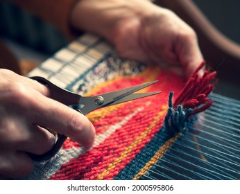 Master weaver is cutting the ends of the threads to create a cut pile carpet effect. Making coloured tapestry, close up