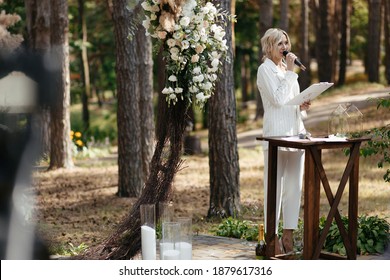 Master of wedding ceremony speeching on microphone on background wedding arch and trees. - Powered by Shutterstock