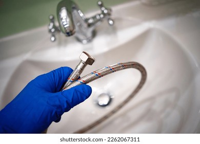 The master's gloved hand holds a chrome bathroom hose.Call the master plumber.