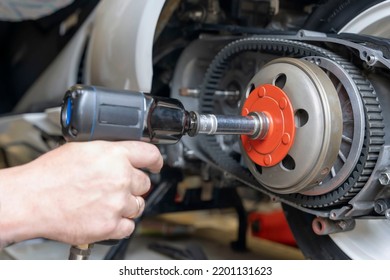 the master's hand unscrews the torque driver nut on the scooter variator using a pneumatic impact wrench. replacement of the transmission pulley belt on the scooter - Powered by Shutterstock