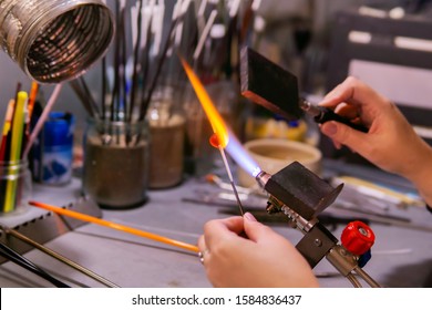 master's hands forming a glass bead with a special paddle during beadmaking in a glass-blowing workshop - Powered by Shutterstock