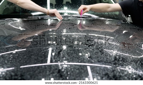 Masters stick a protective film on the hood of the\
car. Car wrapping specialist applied vinyl transparent film on car\
for protection car paint focus on hand of technician. Protection\
film.