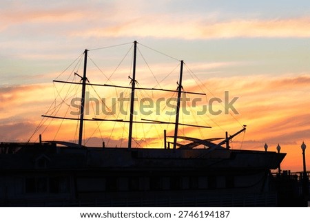 Masts and rigging form a dark outline against a vibrant coastal sky at dusk.
