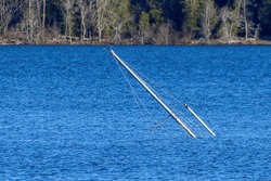 The Masts Of A Sunken Sailboat Sticking Up At An Angle From Blue Water.