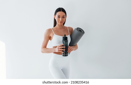 With Mat In Hands. Young Caucasian Woman With Slim Body Shape Is Indoors At Daytime.