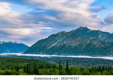 The Matanuska Glacier flows between rugged peaks into a forested valley along the Glenn Highway, Alaska.
