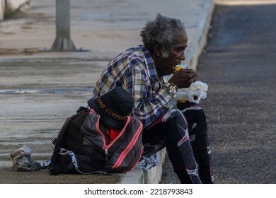 MATANZAS, CUBA - Jul 07, 2022: An Elderly Man Sitting On A Sidewalk And Eating Some Street Food