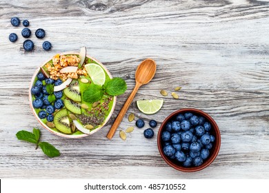 Matcha Green Tea Breakfast Superfoods Smoothies Bowl Topped With Chia, Flax And Pumpkin Seeds, Bee Pollen, Granola, Coconut Flakes, Kiwi And Blueberries. Overhead, Top View, Flat Lay