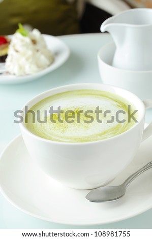 Matcha green tea latte beverage in glass mug with whisk