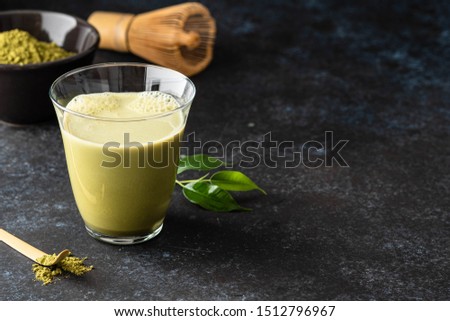 Matcha green tea latte in glass mug with whisk.
