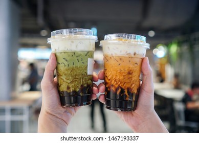 Matcha Green tea and Thai Tea Bubble drinks, man holding a plastic cup of bubble/boba matcha green tea and Thai tea with brown sugar and topped with cheese cream.