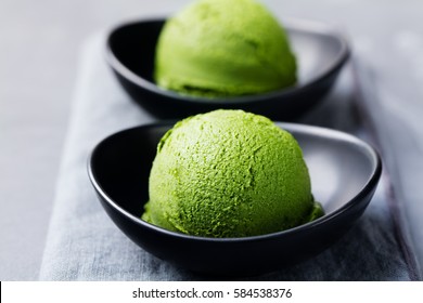 Matcha ice cream scoop in bowl on a grey stone background.