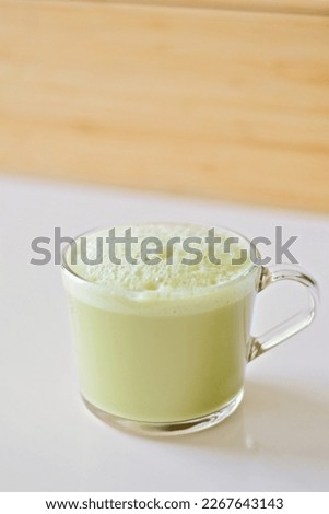 Matcha latte with oatmilk in a glass mug or cup with a neutral and blurry background. Matcha latte is yellow or green in color and has foamy and frothy oatmilk.