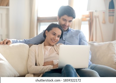 Matching tastes. Loving young husband and wife cuddling on couch at home after workday relaxing resting watching film on laptop computer surfing internet selecting weekend trip on tour company site