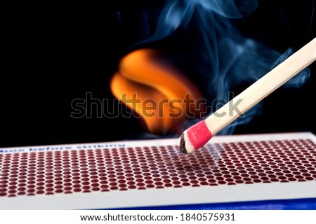 A matchstick lights after it is struck agains the flint surface of a match box.  Everything is real, no flame filters.