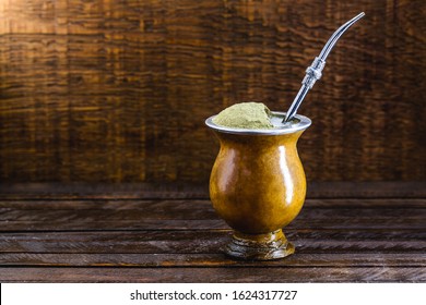 Chimarrão, or mate herb, is a South American drink left by indigenous cultures. It consists of a gourd, a pump, ground yerba mate and boiling water. Chimarrão isolated on wooden background. Copy space