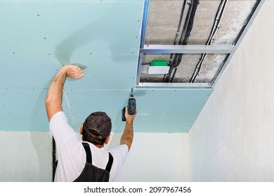 Mater Is Installing A Plasterboard Suspended Ceiling. The Assembly Process Using An Electric Screwdriver Plasterboard Ceiling To The Metal Ceiling Frame. Simple And Affordable Renovation Of Premises