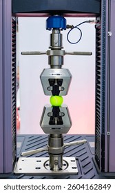 Material testing machine applying pressure on a tennis ball, performing a compression test in a quality control laboratory