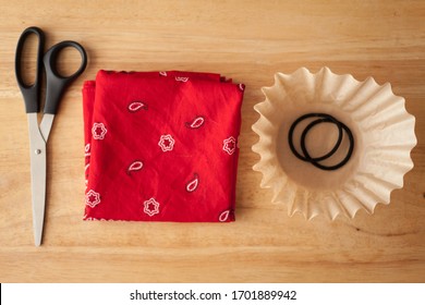 Materials For A Cloth Face Covering, An Easy DIY Face Mask. Flat Lay Of A Bandanna, Scissors, Coffee Filter, And Hair Ties Arranged In A Neat Line.