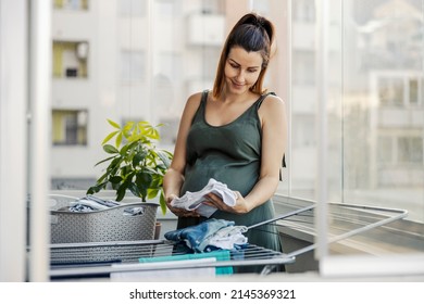 Maternal instinct, house chores and pregnant women. An excited expectant mother prepares clothes for the newborn. A pregnant woman stands on the terrace and prepares clothes for the newborn - Shutterstock ID 2145369321