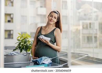 Maternal Instinct, Household Chores And Pregnant Women. An Excited Expectant Mother Prepares Clothes For The Newborn And Poses For A Photo On The Home Balcony. Family Love Motherhood, Tender Look