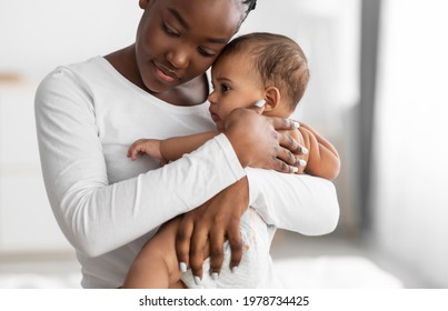 Maternity Concept. Portrait of young African American mother hugging and holding her baby on hands. Displeased infant feeling scared, woman conforting him. Copy space, blurred background