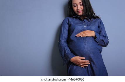 Maternity Fashion Portrait Of Ethnic Woman In Blue Pregnancy Dress Leaning On The Wall - Copy Space - Low Angle Shot